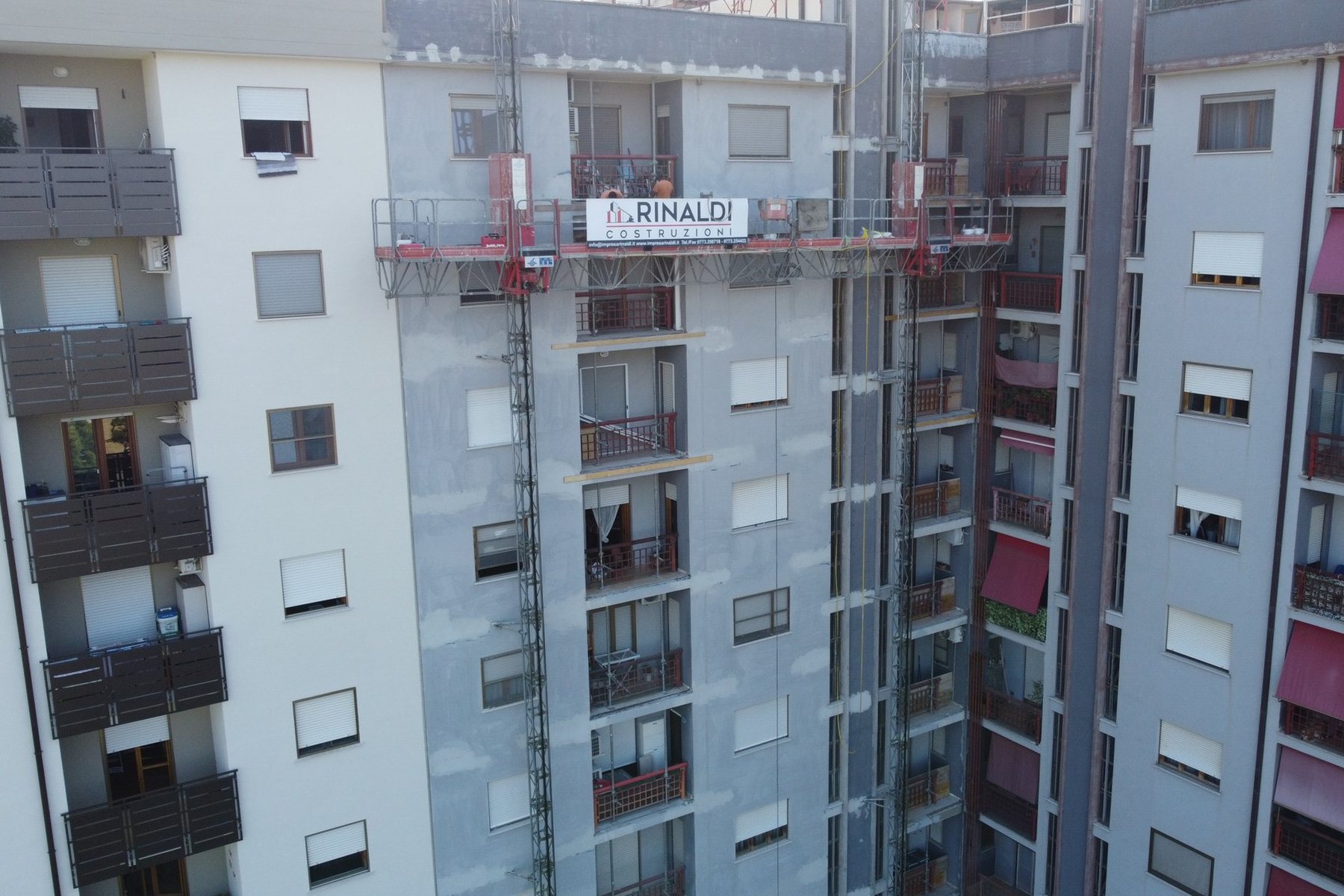 Piattaforma autosollevante Costruzioni Rinaldi con gli operai al lavoro sulla facciata di un condominio a Latina, vista dal drone